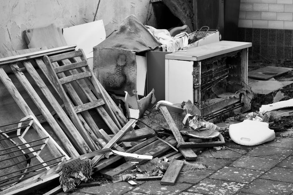 A man with a dark beard and short brown hair is carefully using a screwdriver to disassemble a white crib or small bed frame made of wood with vertical slats. He is wearing a plain white t-shirt and i